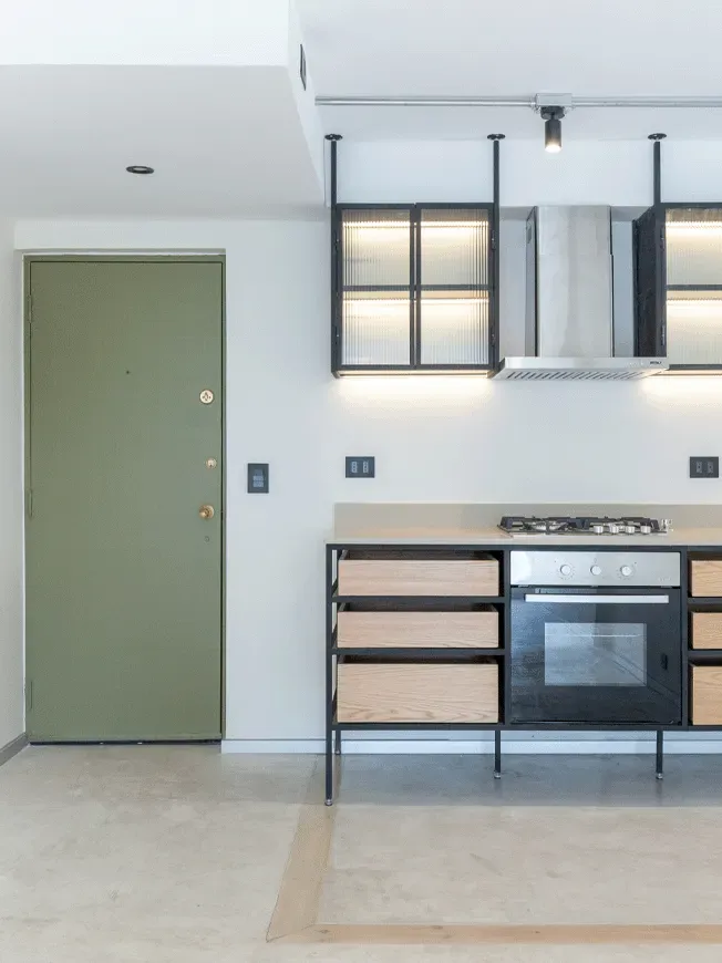Detalle de cocina minimalista en Las Condes con puerta verde oliva, gabinetes industriales con cajones de madera y vitrinas colgantes de vidrio estriado