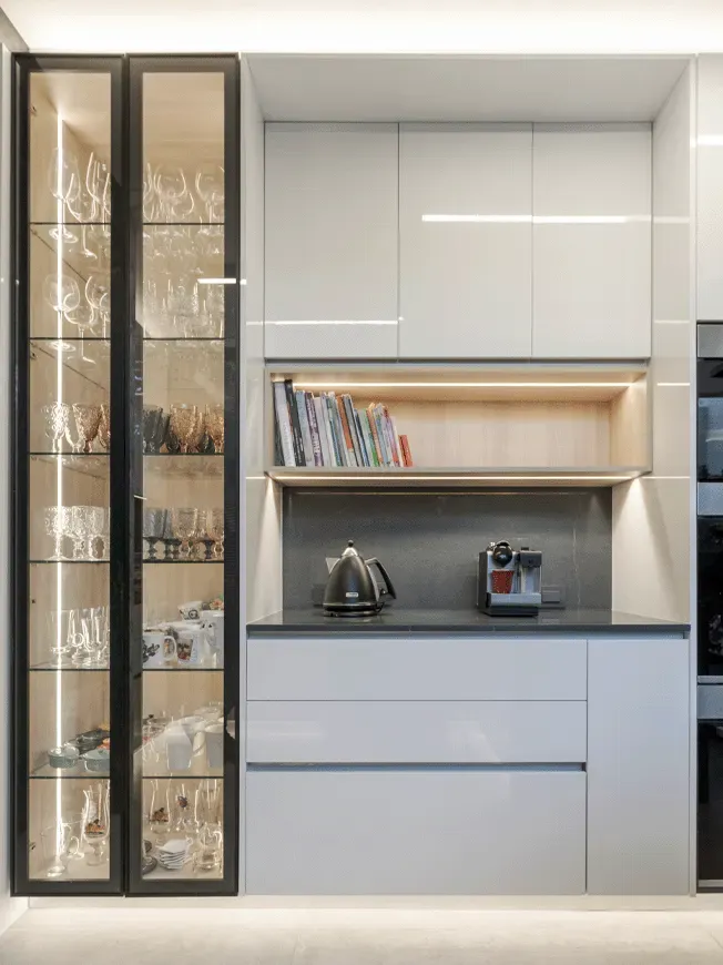 Detalle de cocina moderna en Las Condes con gabinetes blancos, nicho iluminado y vitrina lateral con cristalería