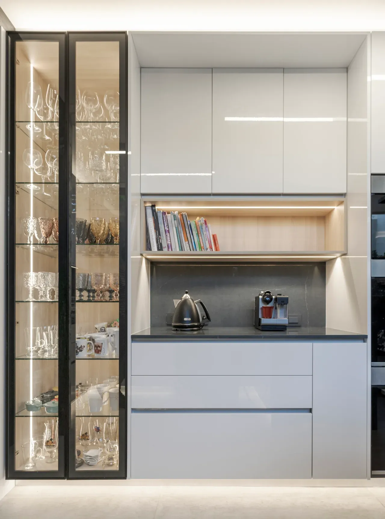 Detalle de cocina moderna en Las Condes con gabinetes blancos, nicho iluminado y vitrina lateral con cristalería