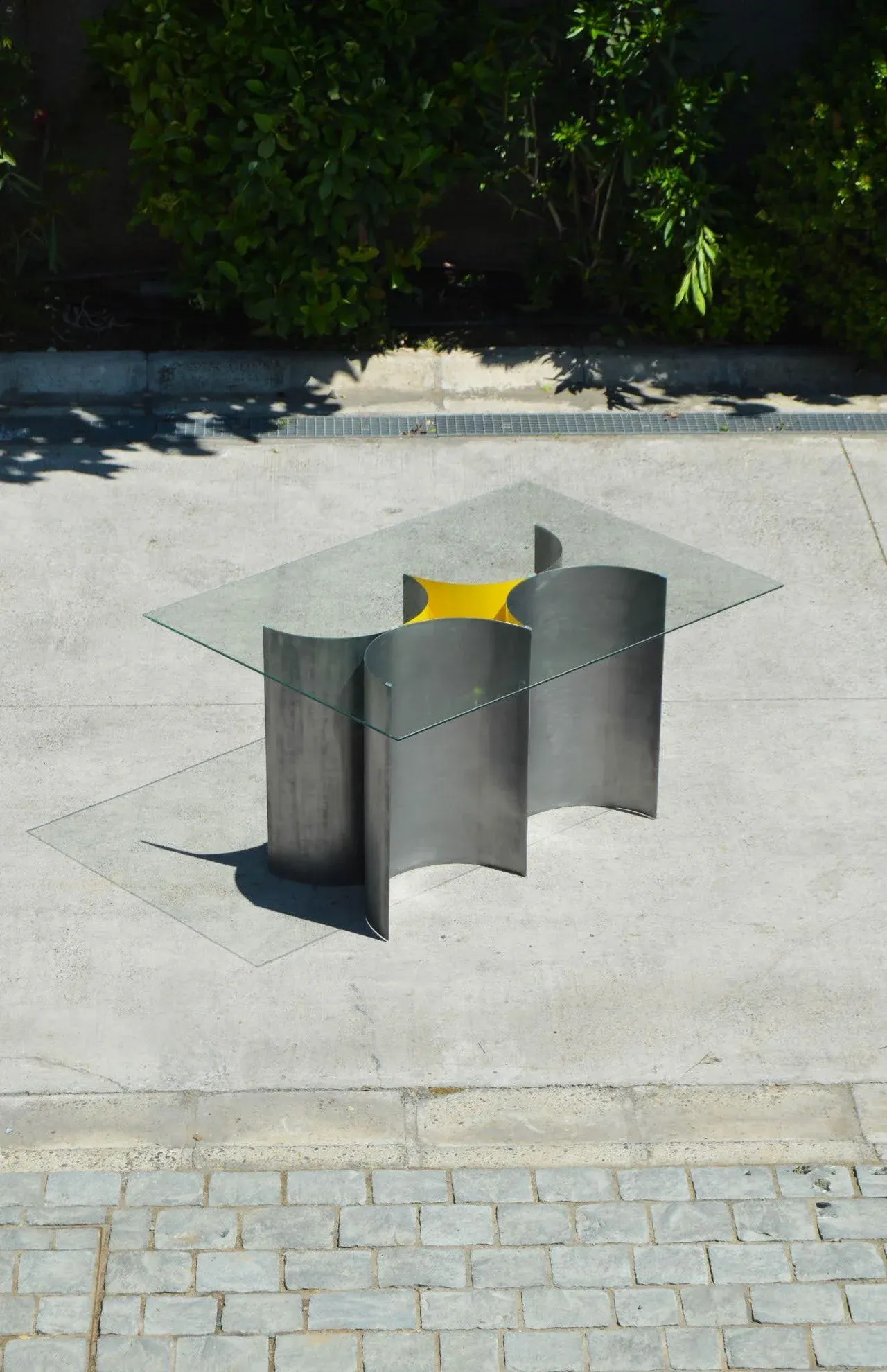 Mesa de centro con base escultórica de acero curvado y tapa cuadrada de vidrio, destacando el diseño de mobiliario moderno