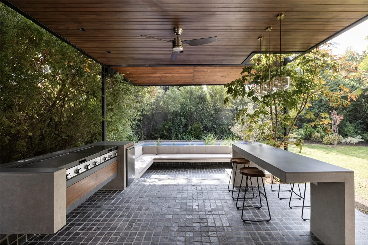 Diseño de quincho moderno en Las Condes con estructura metálica, techo de madera y barra de hormigón integrada en el jardín