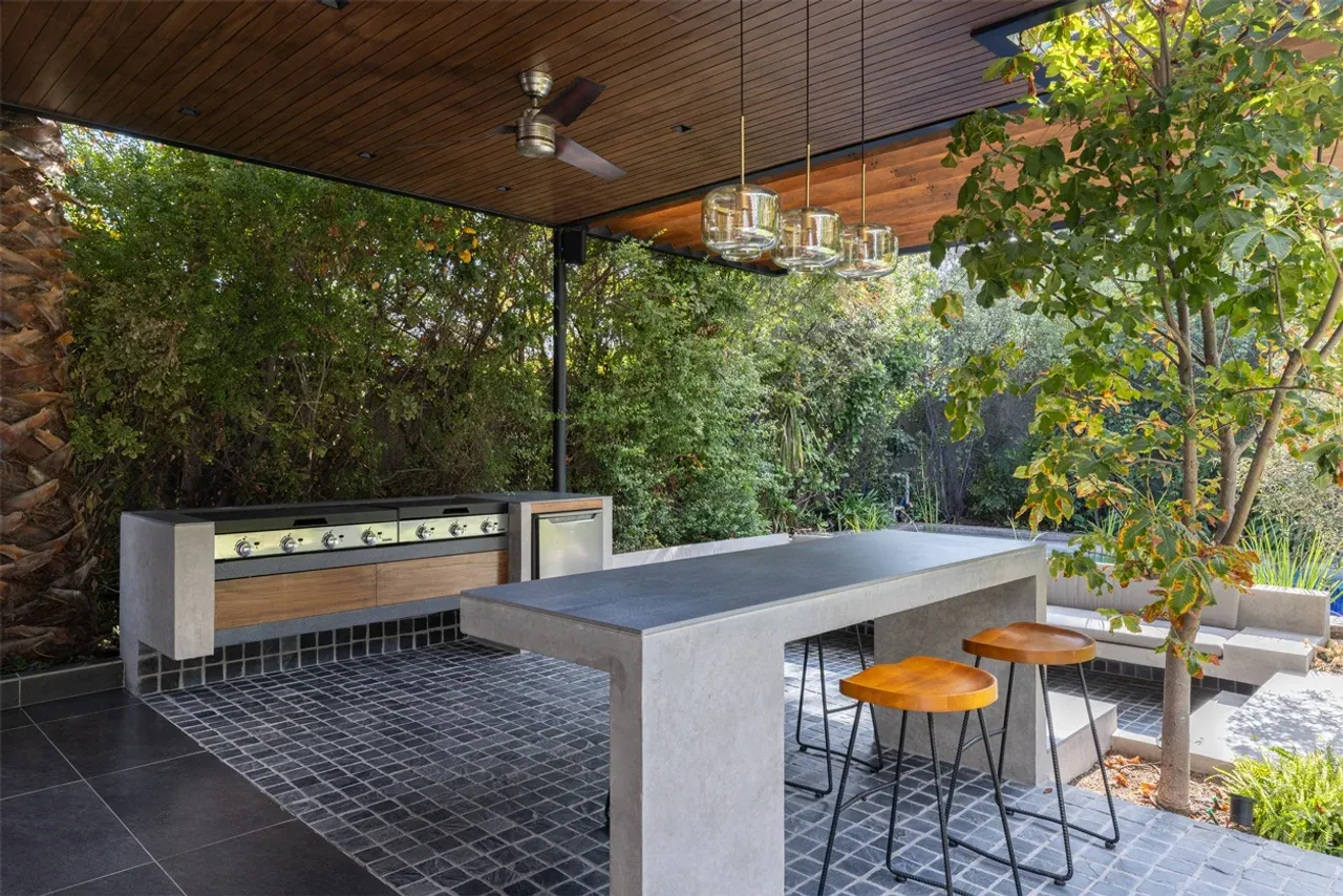 Diseño de quincho moderno en Las Condes con estructura metálica, techo de madera y barra de hormigón integrada en el jardín