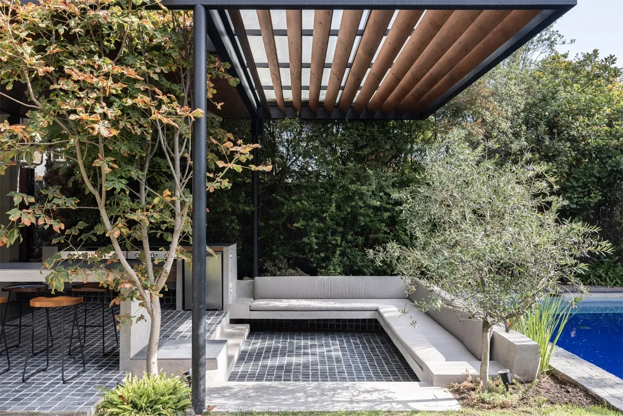 Diseño de quincho moderno en Las Condes con estructura metálica, techo de madera y barra de hormigón integrada en el jardín