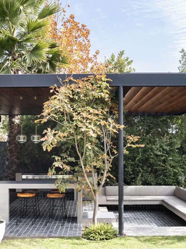 Diseño de quincho moderno en Las Condes con estructura metálica, techo de madera y barra de hormigón integrada en el jardín