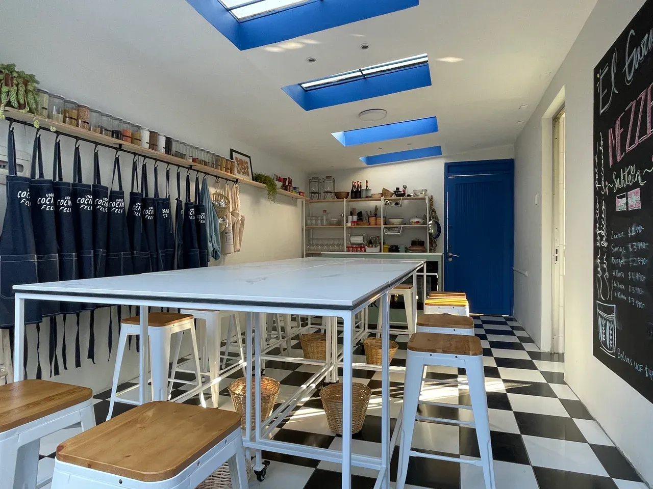 Vista del interior de un garaje transformado en taller de cocina, con mesas de trabajo modular y suelo de baldosas blancas y negras