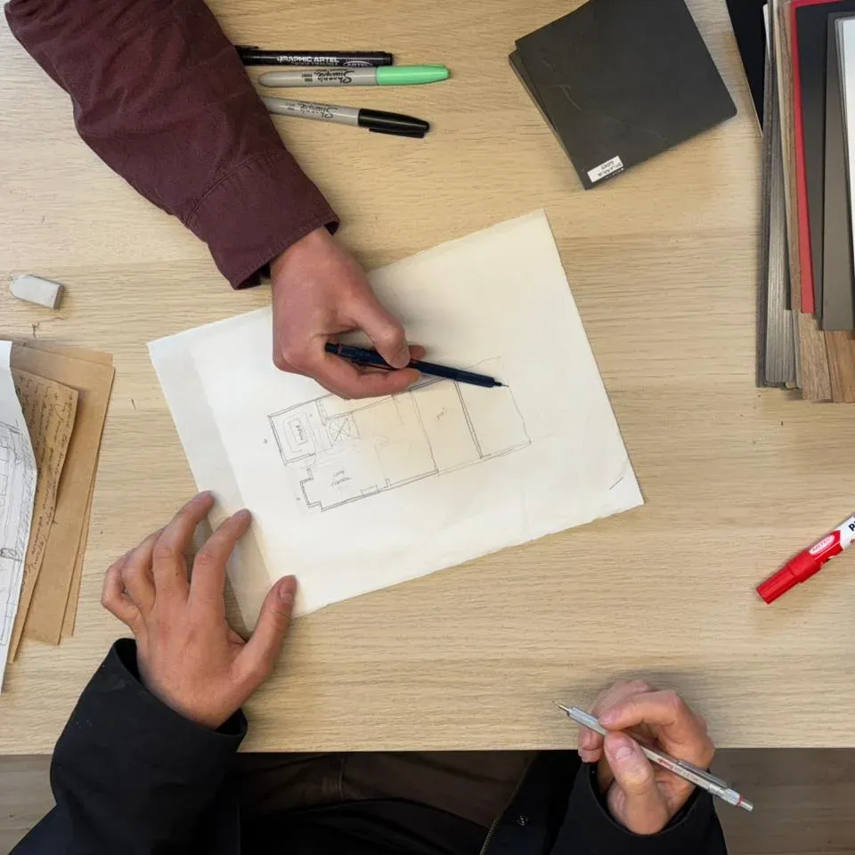 Plano de una casa con dos arquitectos dibujando sobre él