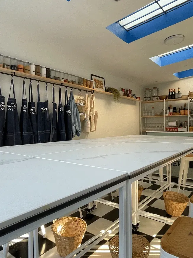 Vista del interior de un garaje transformado en taller de cocina, con mesas de trabajo modular y suelo de baldosas blancas y negras