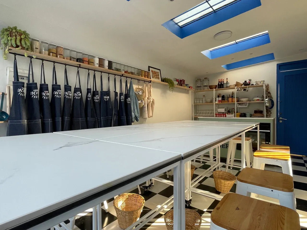 Vista del interior de un garaje transformado en taller de cocina, con mesas de trabajo modular y suelo de baldosas blancas y negras