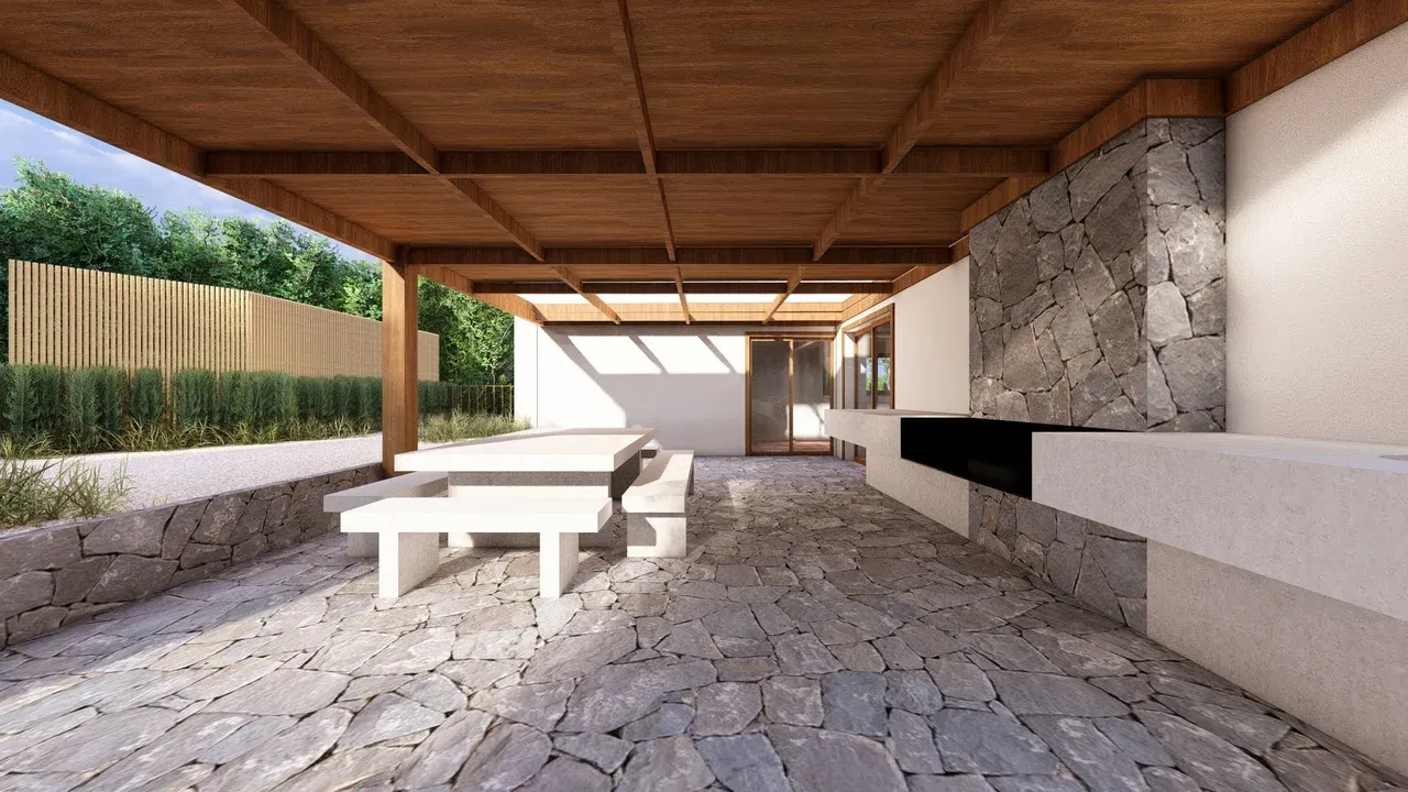 Render 3D de una amplia terraza exterior cubierta en Marbella, con un techo de vigas de madera oscura y un suelo de adoquines de piedra irregulares. La terraza incluye una moderna parrilla empotrada con encimera de concreto y una pared de piedra rústica. Un comedor exterior de concreto blanco se ubica bajo la pérgola.